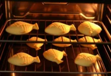 Fish-shaped dough pieces arranged on a parchment-lined baking sheet with the oven door open in the background.